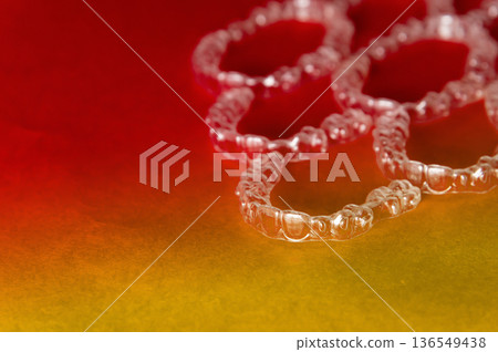 Transparent dental aligners arranged on a gradient background transitioning from red to yellow, showcasing their clear design and unique shape for orthodontic treatment Transparent dental aligners arranged on a gradient background transitioning from red to yellow, showcasing their clear design and unique shape for orthodontic treatment 136549438