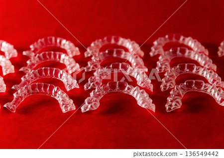 Transparent dental retainers arranged in rows on a vibrant red background, showcasing their clear design and intricate detailing for orthodontic use 136549442