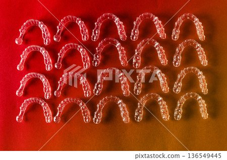 Clear dental aligners arranged in a grid pattern on a gradient background showcasing their transparent design and orthodontic function for teeth straightening 136549445