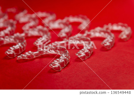 Clear dental aligners arranged on a vibrant red background, showcasing their transparent design and unique shape for orthodontic treatment and teeth straightening 136549448