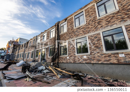 Bila Tserkva, Kyiv region, Ukraine - 09.06.2025: Two story brick building with charred facade, fire damage along the center, and scattered debris on the sidewalk in bright daylight. Bila Tserkva, Kyiv region, Ukraine - 09.06.2025: Two story brick building with charred facade, fire damage along the center, and scattered debris on the sidewalk in bright daylight. 136550011
