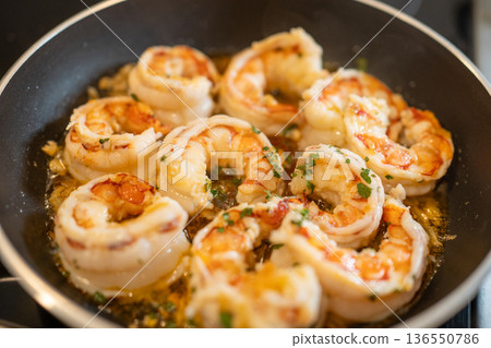 Shrimp sizzling in a hot pan, cooking in a flavorful garlic butter sauce with fresh parsley for a delicious meal 136550786