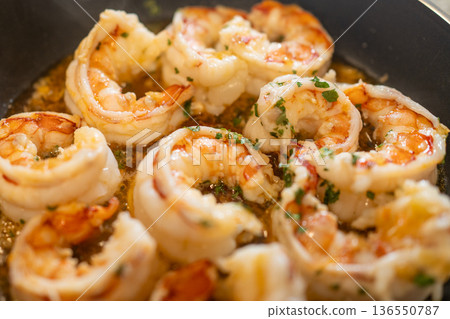 Shrimp scampi cooking in a pan with sizzling garlic, butter, and herbs, preparing a delicious seafood meal 136550787