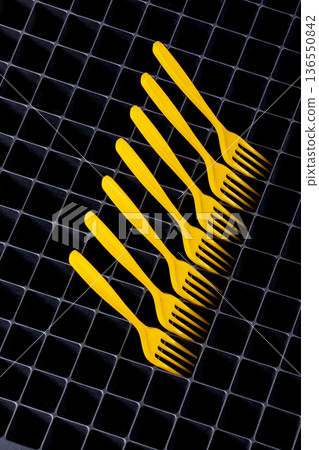 Still life with yellow plastic forks on a surface with cells. Still life with yellow plastic forks on a surface with cells. 136550842