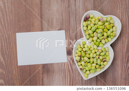 Freshly harvested green olives in heart shaped plate on wooden table, Mediterranean superfood rich in vitamins with blank paper for copy space Freshly harvested green olives in heart shaped plate on wooden table, Mediterranean superfood rich in vitamins with blank paper for copy space 136551096