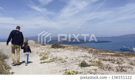 Father and daughter walking along high plateau of Santorini, holding hands, overlooking Aegean Sea, volcanic islands, cruise ship, open sky for text Father and daughter walking along high plateau of Santorini, holding hands, overlooking Aegean Sea, volcanic islands, cruise ship, open sky for text 136551122