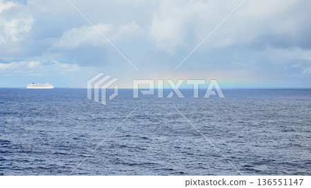 Rare natural phenomenon over open sea with straight horizontal rainbow, deep blue water with ripples, distant cruise ship silhouette under cloudy sky Rare natural phenomenon over open sea with straight horizontal rainbow, deep blue water with ripples, distant cruise ship silhouette under cloudy sky 136551147