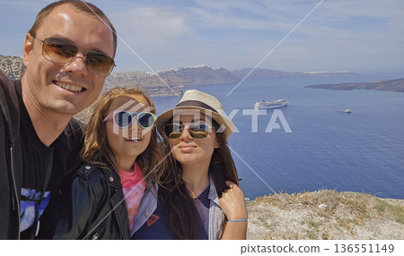 Sunny family selfie with panoramic view of Santorini caldera and Aegean Sea cliffs in bright Mediterranean daylight Sunny family selfie with panoramic view of Santorini caldera and Aegean Sea cliffs in bright Mediterranean daylight 136551149