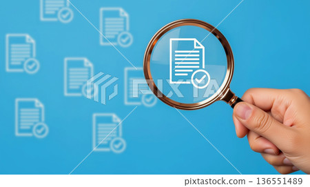 A hand holding a magnifying glass focuses on a document icon with a checkmark, on a blue background with blurred document icons 136551489