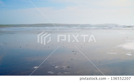 Expansive wet sand beach reflects bright sky with gentle ocean waves in the distance during daytime. Expansive wet sand beach reflects bright sky with gentle ocean waves in the distance during daytime. 136552207