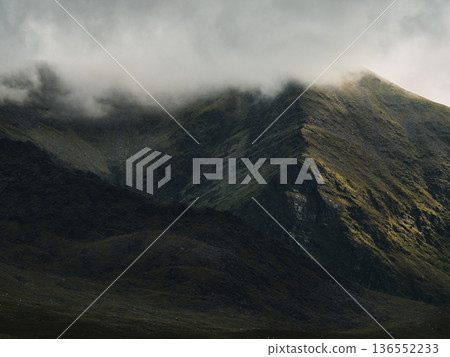 Misty mountains shrouded in atmospheric haze. Sunlight highlights a stark mountain ridge. Misty mountains shrouded in atmospheric haze. Sunlight highlights a stark mountain ridge. 136552233