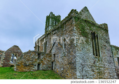 Overcast sky above the historic Timoleague Abbey ruins in County Cork, Ireland. Ancient stone walls, covered in vibrant green moss, feature arched windows. 136552247