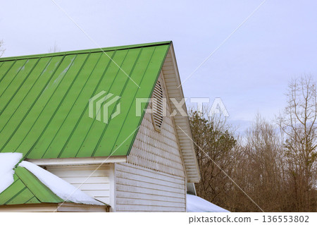 Green metal roof on house reveals winter scene with snow at ground 136553802