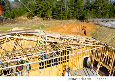 Construction workers build house frame in rural area while machinery is nearby 136553808