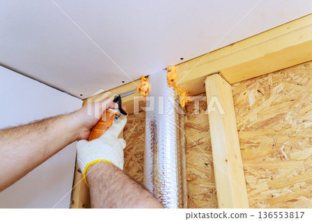 Worker uses spray fire proof foam insulation to seal gap in construction project Worker uses spray fire proof foam insulation to seal gap in construction project 136553817