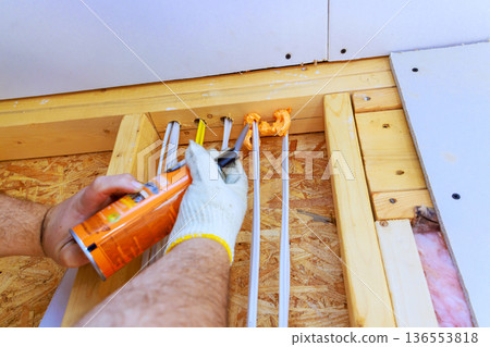 Worker applies fire proof sealant to wood structure in home improvement project 136553818