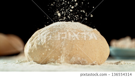 Static shot of a leavened dough loaf isolated on black background with falling flour. Concept of baking, artisan bread making and dough preparation. 136554314