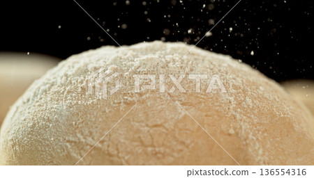 Static shot of a leavened dough loaf isolated on black background with falling flour. Concept of baking, artisan bread making and dough preparation. Static shot of a leavened dough loaf isolated on black background with falling flour. Concept of baking, artisan bread making and dough preparation. 136554316