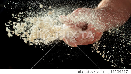 Closeup of bakers hand throwing flour against black background. Dramatic flour explosion captured in high detail, baking and culinary preparation concept. 136554317