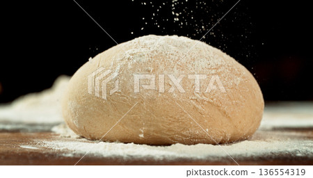 Static shot of a leavened dough loaf isolated on black background with falling flour. Concept of baking, artisan bread making and dough preparation. 136554319
