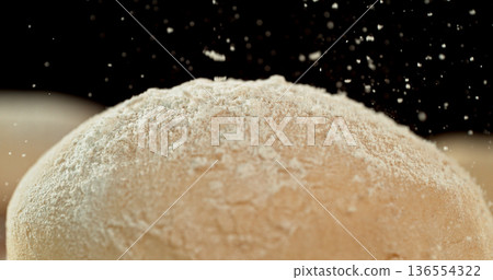 Static shot of a leavened dough loaf isolated on black background with falling flour. Concept of baking, artisan bread making and dough preparation. Static shot of a leavened dough loaf isolated on black background with falling flour. Concept of baking, artisan bread making and dough preparation. 136554322