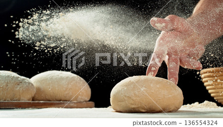 Close up of bakers hand tossing flour over prepared risen dough on wooden table. Cinematic baking concept, artisan bread preparation and texture detail. Close up of bakers hand tossing flour over prepared risen dough on wooden table. Cinematic baking concept, artisan bread preparation and texture detail. 136554324