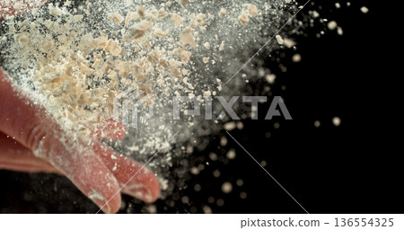 Closeup of bakers hand throwing flour against black background. Dramatic flour explosion captured in high detail, baking and culinary preparation concept. 136554325