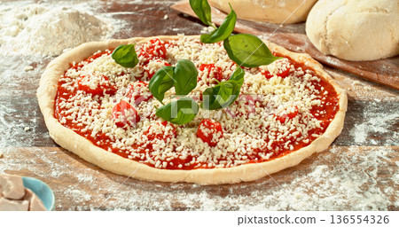 Shot of fresh basil leaves falling onto raw pizza dough topped with tomato sauce and mozzarella. Cinematic detail of Italian pizza preparation on a floured wooden table. Shot of fresh basil leaves falling onto raw pizza dough topped with tomato sauce and mozzarella. Cinematic detail of Italian pizza preparation on a floured wooden table. 136554326