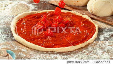 Fresh sliced tomatoes falling into rich tomato sauce on raw pizza dough. Cinematic food preparation shot capturing splash, texture and motion in detail. 136554331