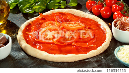 Fresh sliced tomatoes falling into rich tomato sauce on raw pizza dough. Cinematic food preparation shot capturing splash, texture and motion in detail. 136554333
