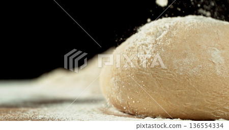 Static shot of a leavened dough loaf isolated on black background with falling flour. Concept of baking, artisan bread making and dough preparation. 136554334