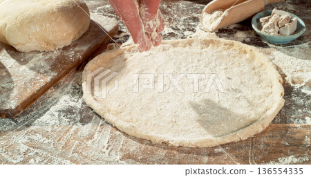 Falling flour dusting freshly kneaded pizza dough on wooden table. Cinematic baking concept, preparation of homemade pizza and yeast dough. 136554335