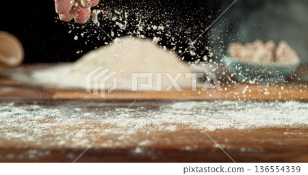 Close up of bakers hand tossing flour over prepared risen dough on wooden table. Cinematic baking concept, artisan bread preparation and texture detail. 136554339