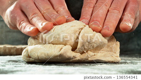 Closeup of a bakers hands kneading and stretching freshly risen dough. Detailed texture and elasticity visible in cinematic light. Concept of yeast dough preparation and traditional baking process. Closeup of a bakers hands kneading and stretching freshly risen dough. Detailed texture and elasticity visible in cinematic light. Concept of yeast dough preparation and traditional baking process. 136554341
