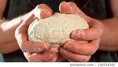 Closeup of a bakers hands kneading and stretching freshly risen dough. Detailed texture and elasticity visible in cinematic light. Concept of yeast dough preparation and traditional baking process. 136554342