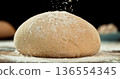 Static shot of a leavened dough loaf isolated on black background with falling flour. Concept of baking, artisan bread making and dough preparation. 136554345