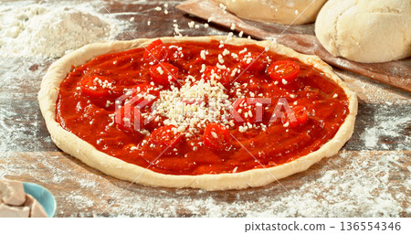Closeup of grated mozzarella falling onto fresh pizza with tomato sauce and sliced tomatoes. Detailed texture, flying cheese particles and dynamic motion. Concept of pizza preparation and cooking. 136554346