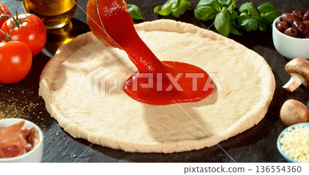 Closeup of spreading tomato sauce on fresh pizza dough. Spoon moves gently across the surface, highlighting texture, freshness and authentic Italian pizza preparation. Closeup of spreading tomato sauce on fresh pizza dough. Spoon moves gently across the surface, highlighting texture, freshness and authentic Italian pizza preparation. 136554360