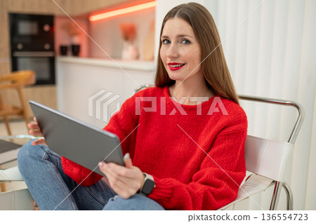 Beautiful young woman in red with a laptop at home Beautiful young woman in red with a laptop at home 136554723