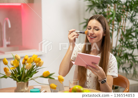 Smiling young long-haired woman doing make up and looking excited 136554853