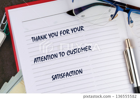 An open notebook displays a thank you message for customer satisfaction. Eyeglasses and a silver pen rest on the pages next to the text An open notebook displays a thank you message for customer satisfaction. Eyeglasses and a silver pen rest on the pages next to the text 136555582
