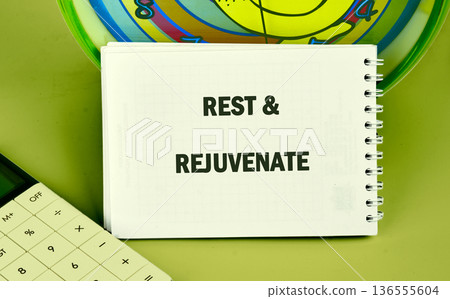 A note saying rest and rejuvenate is on a table next to a calculator and a colorful clock. The setting shows a workspace with a simple layout 136555604