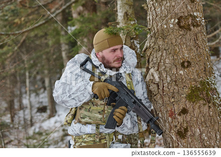 Soldier In Winter Camouflage Holding Rifle Behind Tree In Snowy Forest Tactical Patrol 136555639