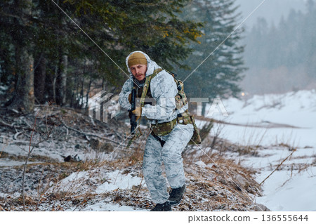 Soldier In White Winter Camouflage Patrolling Snowy Forest With Rifle And Tactical Gear 136555644