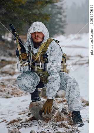Armed Soldier In Winter Camouflage Crouching With Rifle And Tactical Gear In Snowy Forest 136555655