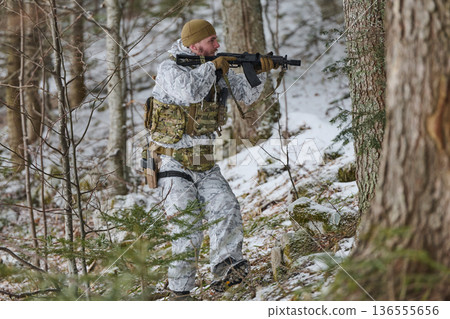 Soldier in White Winter Camo Moving Through Snowy Forest With Rifle and Tactical Gear 136555656