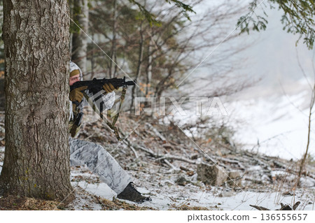 Soldier in Winter Camouflage Aiming Rifle Behind Tree in Snowy Forest During Training 136555657