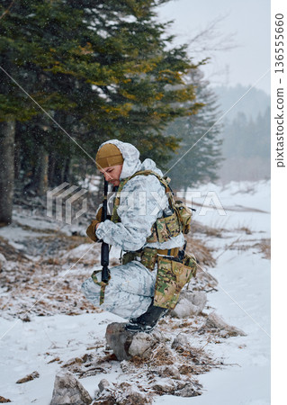 Soldier In Winter Camouflage Kneeling With Rifle On Snowy Forest Edge During Patrol 136555660