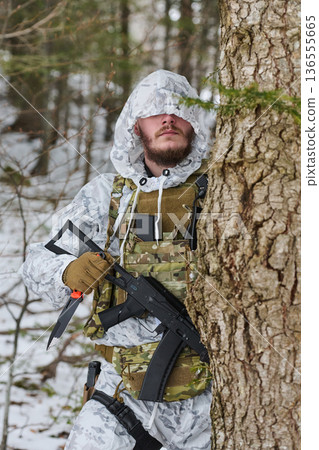 Soldier In Winter Camouflage With Rifle And Knife Hiding Behind Tree In Snowy Forest Soldier In Winter Camouflage With Rifle And Knife Hiding Behind Tree In Snowy Forest 136555665