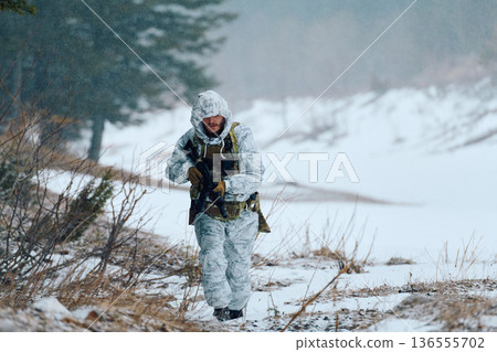 Soldier in White Winter Camouflage Patrols Snowy Forest With Rifle During Cold Weather Operation 136555702
